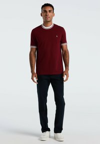 Bordeaux katoenen T-shirt met witte ribgebreide kraag en mouwaccenten. Draagt met een marineblauwe broek en witte sneakers. Geen zichtbare patronen of grafische elementen.