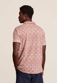 Korte mouwen polo shirt met een rood en beige golvende bladerenpatroon, met een contrasterende kraag in blauw en roze accenten. Katoenen materiaal.