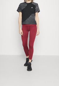 Camiseta deportiva negra con patrón triangular blanco, combinada con leggings ajustados burdeos y zapatos deportivos negros.