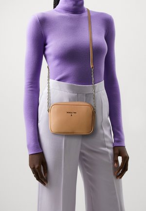 Persona vestida con un suéter de tortuga lavanda y pantalones gris claro, llevando un pequeño bolso cruzado color beige con una cadena y correa de cuero.