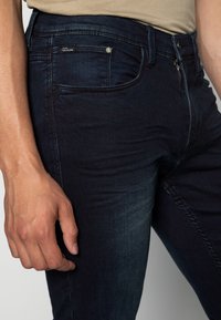 Mörkblå denimjeans med en figurnära design, utrustade med framfickor, dragkedjefly, och lätt blekning på lårområdet.