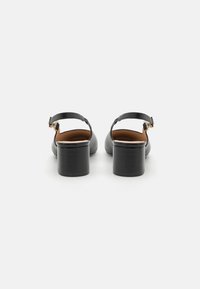 Sorte lærblokk-hæl sko med slingback-design, med en gullfarget spenne og myk brunt interiør. Jevn tekstur og minimalistisk stil.