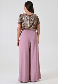 Pailletten top in brons met roze wijde broek. De top heeft korte mouwen en een sleutelgat aan de achterkant; de broek is glad met een elastische tailleband.