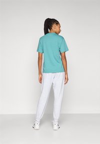 Teal puuvillane T-särk lühikeste varrukatega, koos hallide dressipükstega. Mudel kannab valgeid sportlikke jalanõusid mustade detailidega.