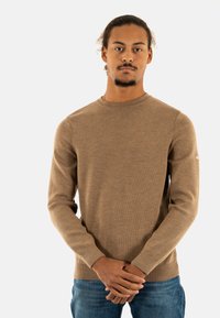 Maglione marrone a maniche lunghe con colletto rotondo, polsini a coste e lavorazione a maglia testurizzata. Abbinato a jeans in denim blu.