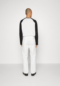 Camicia a maniche lunghe con maniche raglan nere e corpo bianco, abbinata a pantaloni bianchi. Design semplice con una vestibilità comoda.