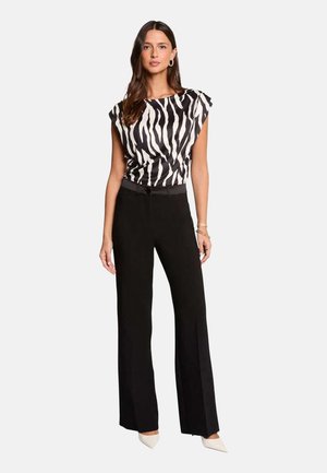 Femme portant un haut sans manches à imprimé zèbre noir et blanc, un pantalon large taille haute noir, et des chaussures blanches pointues.