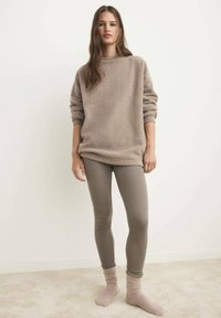 Beige fleece sweatshirt met een ronde hals en ribgebreide manchetten, gecombineerd met taupe leggings en lichtroze sokken, op een model tegen een neutrale achtergrond.
