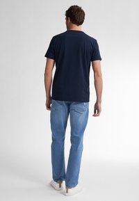 Mornarsko moder kratkolasni T-shirt s okruglim izrezom, uparen s svijetlosmodrim ravnim trapericama i bijelim tenisicama s smeškastim akcentima.