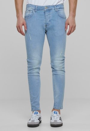 Jeans de mezclilla azul claro con un corte slim, que presentan un ligero desgaste y detalles de costura, combinados con zapatillas deportivas blancas.