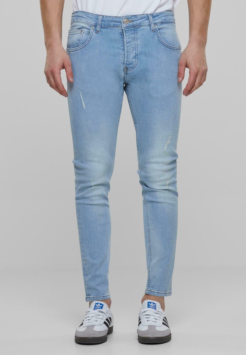 Fénykék farmernadrág, slim fit szabással, finom kopásos és varrási részletekkel, fehér sportcipővel párosítva.