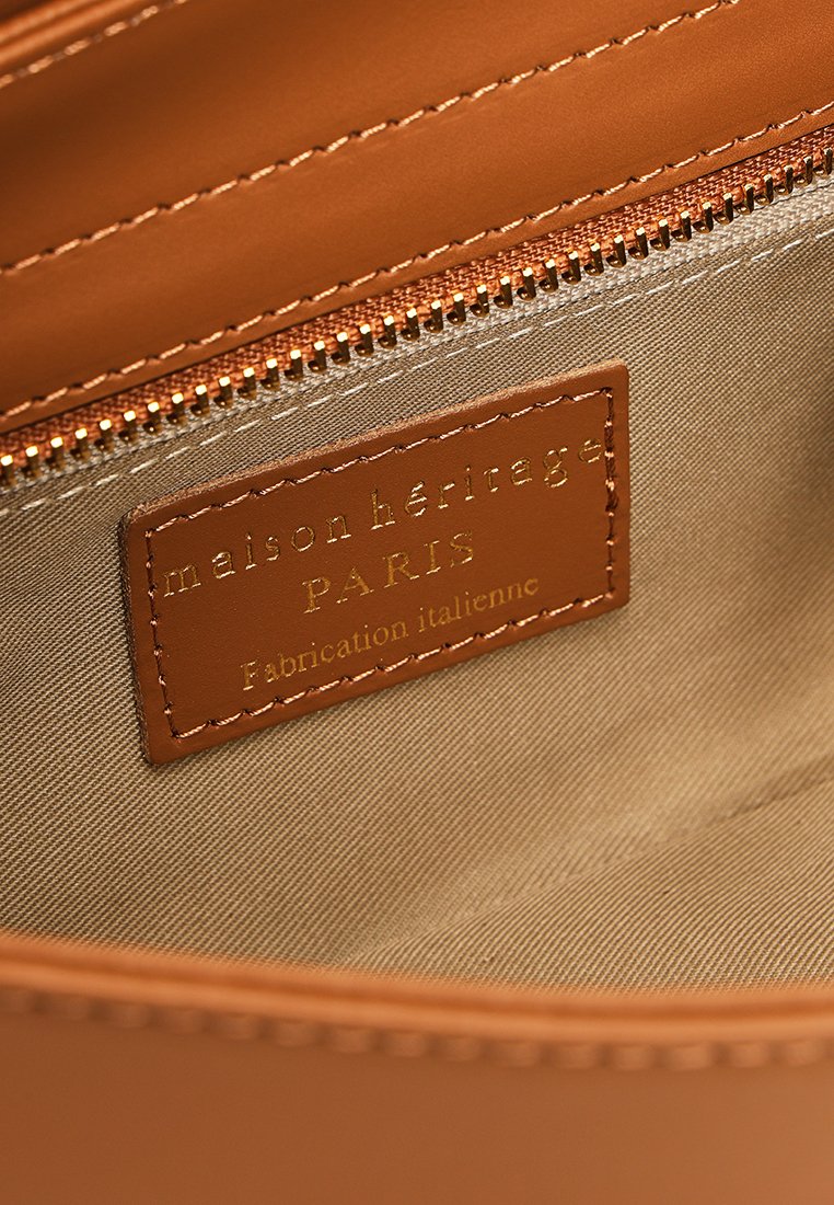 Braunes Lederinterieur einer Handtasche mit einem goldgeprägten Etikett, auf dem "maison héritage PARIS" steht, beige Stoffauskleidung und einem Reißverschluss.