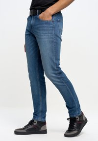 Mörkblå denimjeans för män med smal passform, med framfickor och en mjuk textur. Kombinerat med svarta och grå högskor.
