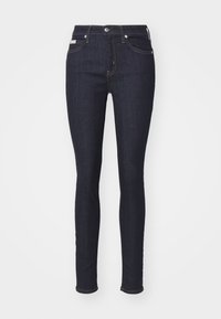 Temno modre usnjene skinny hlače z visokim pasom, petimi žepi in kontrastnim šivom. Imajo zadrgo in zanke za pas.