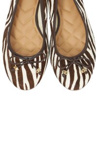 Chaussures plates en imprimé zèbre avec texture de fourrure marron et blanche. Bout arrondi, accents marron, petit nœud et détails décoratifs en métal.