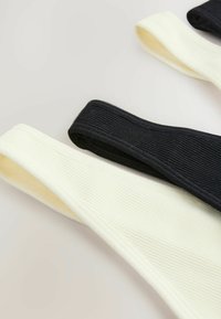 Set med tre elastiska hårband i ribbat tyg: två i ljusgul, en i svart, med släta kanter och en sömlös design.