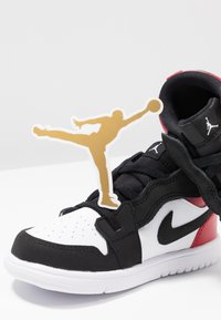 Baskets montantes Nike Air Jordan noires, blanches et rouges avec des lacets noirs et une silhouette du logo Jumpman doré sur fond blanc.