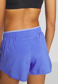 Blaue Sportshorts aus glattem Material, mit einem elastischen Bund und einer kleinen Gesäßtasche. Die Shorts haben einen lockeren Sitz und einen abgerundeten Saum.