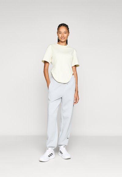 Light yellow short-sleeve t-shirt with a round hem, paired with light gray sweatpants and white sneakers with black accents.