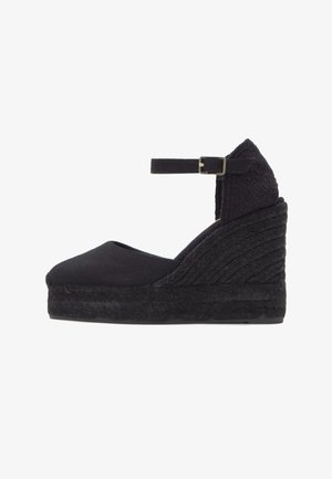 Espadrille compensée noire avec bout fermé, bride à la cheville et semelle plateforme tressée texturée.
