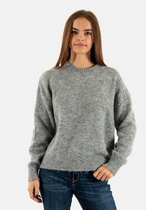 Pull en tricot gris avec un col rond et des poignets côtelés. Le tissu a une apparence douce et texturée, associé à un jean bleu.