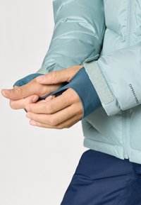 Απαλή γαλάζια φουσκωτή ζακέτα με γάντι που εφαρμόζει στον καρπό. Το μανίκι διαθέτει ρυθμιστική ταινία velcro. Λεια, γυαλιστερή ύφανση χωρίς σχέδια.