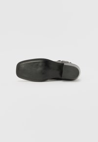 Suela de sandalia negra con una textura lisa, forma plana y sutiles acentos grises. Presenta una suela exterior de goma flexible para mayor tracción.