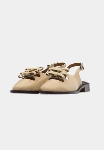 Μπεζ μπαλαρίνες slingback με μυτερή μύτη και διακοσμητικά φιόγκους στην κορυφή, με χαμηλά σκούρα καφέ τακούνια σε λευκό φόντο.