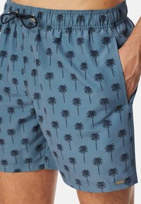 Simshorts i blått tyg med ett mönster av palmträd, elastisk midja med dragsnöre och sidofickor. Slen struktur.