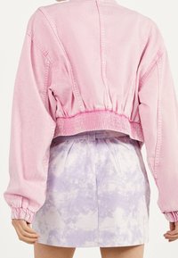 Person som bär en rosa kort jacka med dragsko i midjan och ärmar, kombinerad med en högmidjad lila och vit tie-dye kjol.