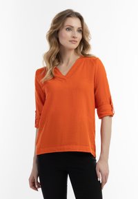 Orange V-hals-bluse med trekvartærmer, opkr�øllede manchetter og løs pasform. Tekstureret stof, lige kant og elegant enkelhed.