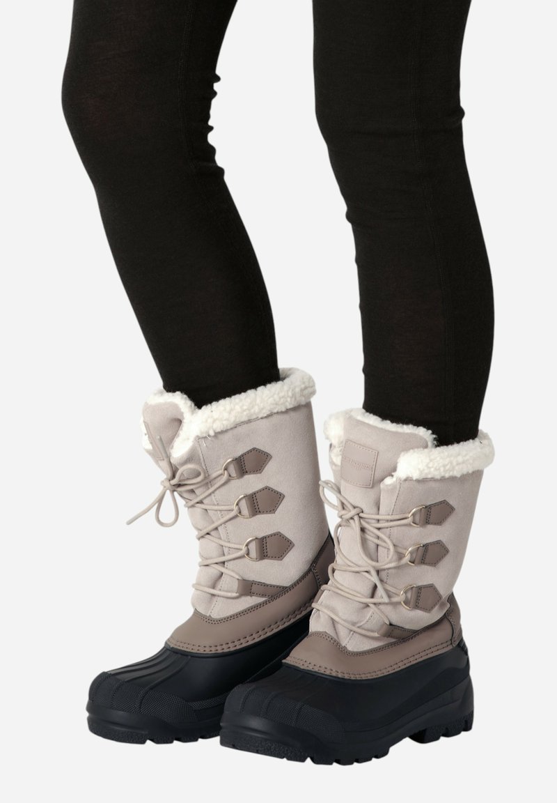 Botas de invierno con parte superior en beige, forro de piel sintética, suela de goma negra y sistema de cordones con ganchos de metal y detalles de cuero.