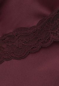 Burgundowa satynowa tkanina z delikatnym ciemno-burgundowym koronkowym wykończeniem z misternymi wzorami kwiatowymi wzdłuż jednego brzegu. Gładka tekstura i elegancki design.