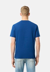Camiseta de algodón azul con mangas cortas, cuello redondo y una textura lisa. Llevada con vaqueros de mezclilla azul claro. Vista trasera.