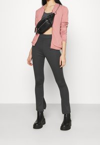 Giacca bomber rosa, top grigio corto, leggings grigi a vita alta e stivali neri con piattaforma. Borsa a tracolla nera con dettaglio zip.