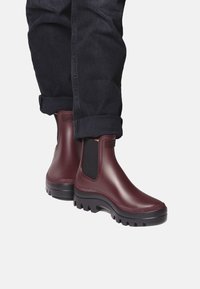 Bottes en caoutchouc bordeaux pour la cheville avec des panneaux latéraux élastiques, semelles noires texturées, design courbé et finition lisse et brillante.