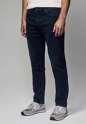 Dark blue jeans with a slim fit, made of denim, featuring a classic five-pocket design and subtle stitching details, paired with gray sneakers.