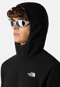 Czarny polarowy hoodie z dopasowanym kapturem, z białym logo "The North Face" na klatce piersiowej. Nosi także białe i czarne okulary przeciwsłoneczne.