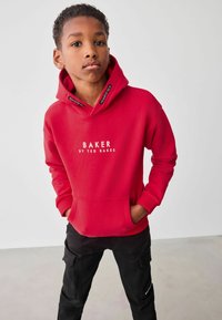 Sudadera roja hecha de tela suave con un bolsillo frontal; presenta "BAKER BY TED BAKER" en texto blanco, cordones negros y puños de canalé.