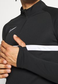 Nike black half-zip long-sleeve top with white stripe at chest. Made of lightweight fabric, features fitted sleeves with thumbholes.