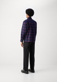 Langermet skjorte med et blått og rødt geometrisk mønster, kombinert med sorte bukser og svarte sko. Stoffet virker glatt og lett.
