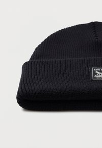 Musta ribbed neulepipo karkean taitoksella ja pienellä suorakaiteen muotoisella Levi's-merkinnällä taitoksessa valkoista taustaa vasten.