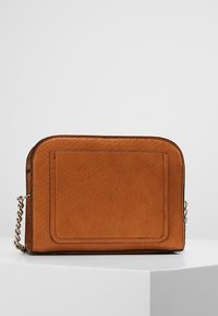 Tan læder crossbody taske med en tekstureret overflade, rektangulær form og en kædestropp. Har en simpel frontlomme uden hardware detaljer.