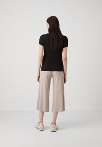 Haut noir à manches courtes côtelé associé à un pantalon cropped beige texturé et des baskets blanches avec des accents orange, vu de dos.