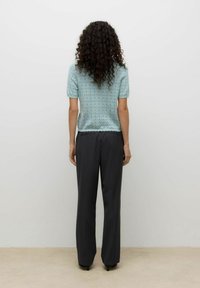 Jasnoniebieski top z krótkim rękawem, z falowanym dołem i teksturowanym wzorem, w zestawieniu z szerokimi spodniami w ciemnoszarym kolorze. Prosty krój, bez zdobień.