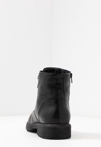 Svart läderankelboot med rund tå, slät yta, dragkedja bak och låg gummihäl. Synlig sömnadsdetalj.