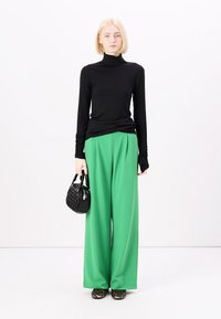 Haut à col roulé noir à manches longues, pantalons larges verts, sac à main texturé noir et chaussures à imprimé léopard. Design simple avec des couleurs vives.