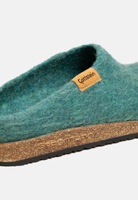 Zoccolo slip-on in felt verde-blu con suola in sughero, impresso con "Stegmann" e un piccolo etichetta marrone chiaro con la scritta "Gottstein" sul lato superiore.