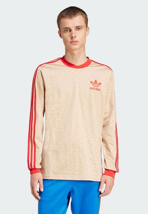 Beige garais piedurkņu krekls ar teksturētu rakstu, sarkaniem akcentiem apkaklītē un piedurkņos, ar Adidas logo uz krūšu daļas.