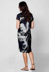 Vestido negro de manga corta con un diseño floral blanco, tejido suave, corte a la altura de la rodilla y aberturas laterales. Combinado con sandalias marrones de tiras.